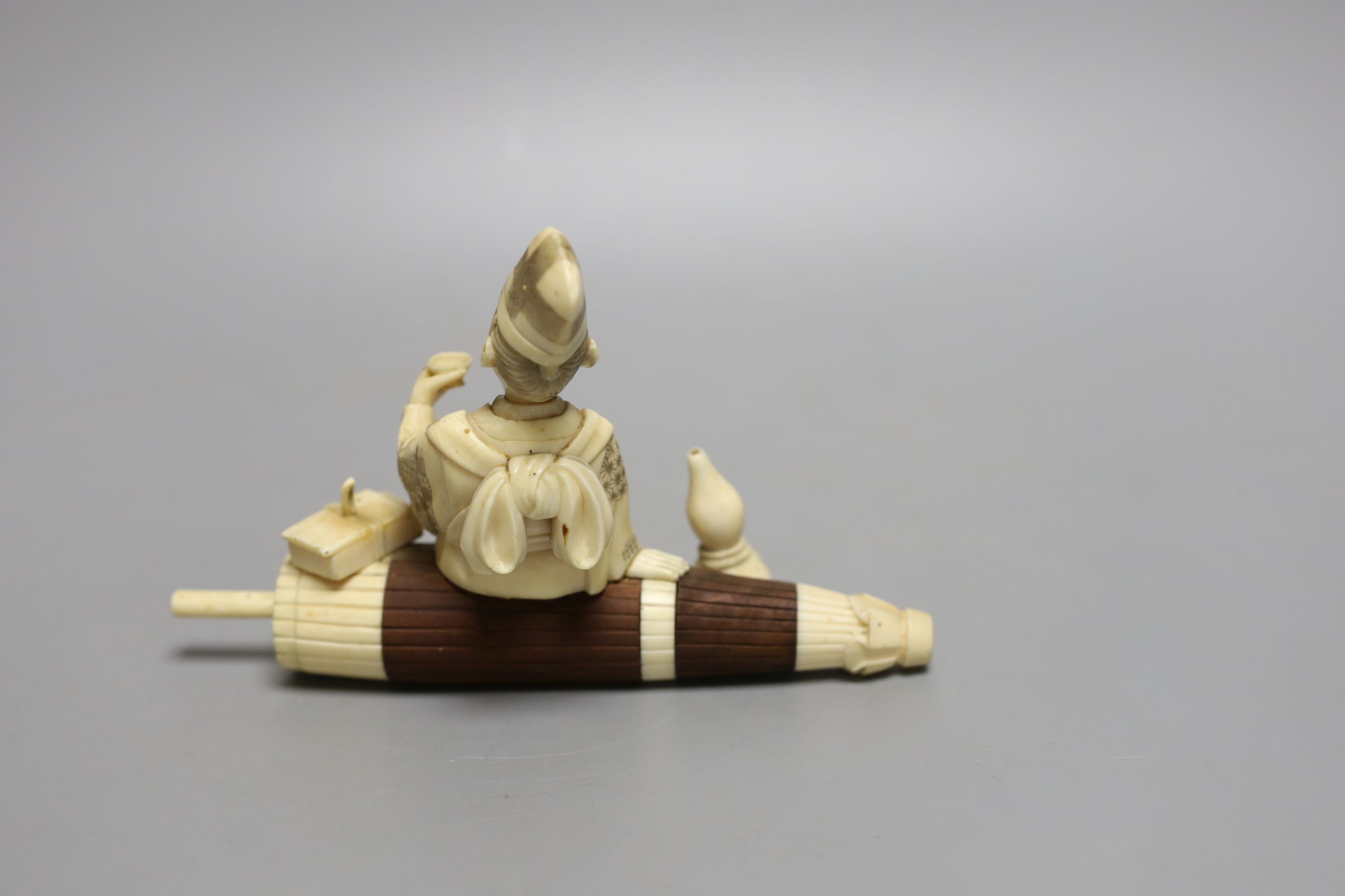 A Japanese ivory and wood okimono of a priest seated on a parasol, early 20th century, signed to a red lacquer tablet - 11cm tall